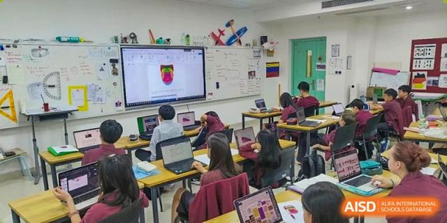 A classroom with multiple students working on laptops while viewing content displayed on a large interactive screen at Canadian International School of Hefei.