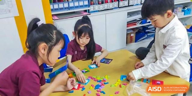 A student working with colorful building blocks at a table in a classroom with storage shelves in the background at Canadian International School of Hefei.