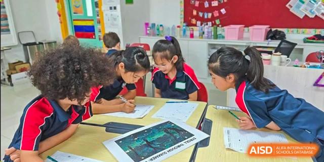 Younger students gathered around a desk, writing and using an illuminated tablet for a group project at Canadian International School of Hefei.