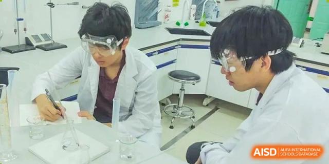 Two students wearing safety goggles and lab coats discussing an experiment in a modern science laboratory at Canadian International School of Hefei.