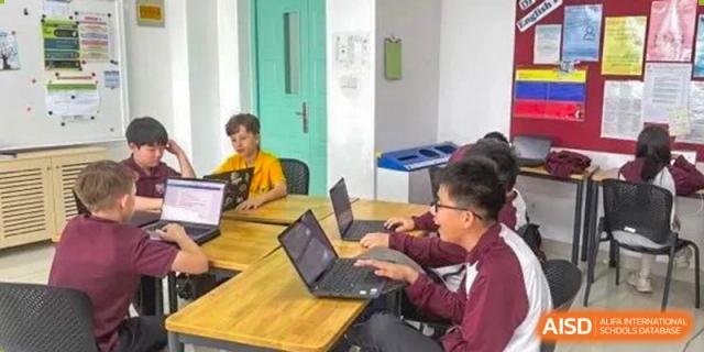 A small group of students collaborating while working on laptops at a yellow desk at Canadian International School of Hefei.