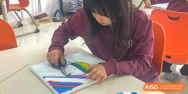 A female student focused on cutting or manipulating colorful paper for an art project at Canadian International School of Hefei.