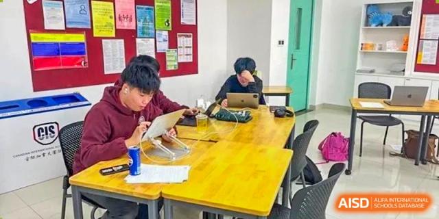 A group of students working together on a project at a long yellow table in a classroom at Canadian International School of Hefei.