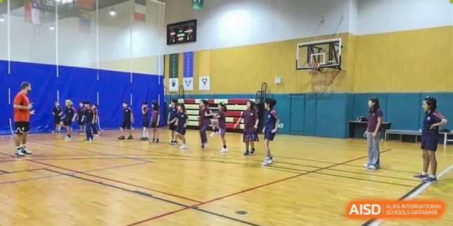 Students standing in formation on a hardwood gymnasium floor near a basketball hoop at Canadian International School of Hefei.