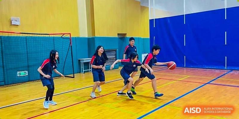 Two students running and lunging to tag or chase a third student on a gymnasium floor at Canadian International School of Hefei.