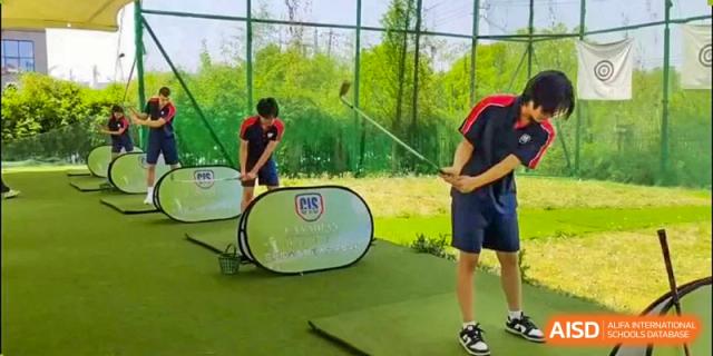 Two students practicing a golf swing outdoors near a driving mat and net at Canadian International School of Hefei.