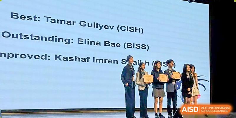 An award ceremony on stage with adults and students, with a screen in the background listing student names from CISH and BISS at Canadian International School of Hefei.