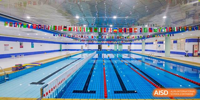 An indoor Olympic-sized swimming pool with multiple lanes and a ceiling decorated with international flags at Canadian International School of Hefei.