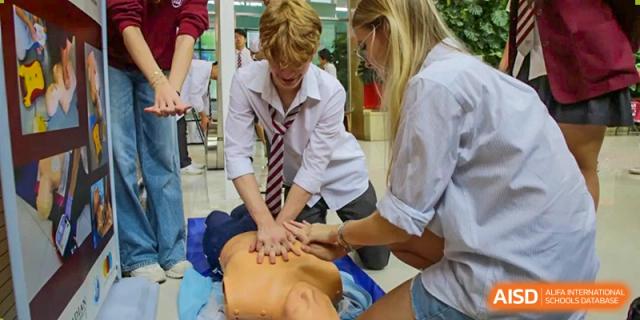 A student practicing first aid or spinal compression techniques on a classmate under the supervision of a teacher or professional at Canadian International School of Hefei.