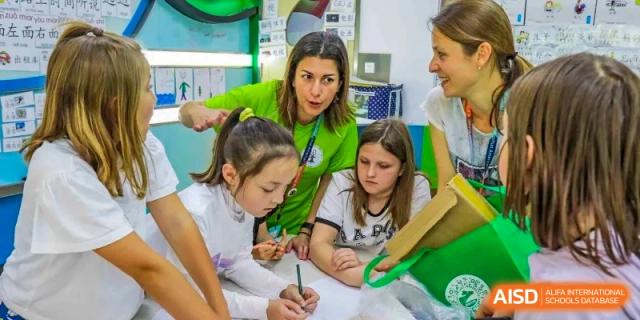 A female teacher from Changchun American International School (CAIS) assisting two young female students with a written assignment.
