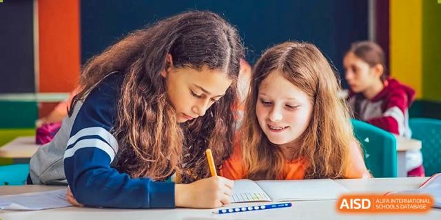Two female students from Changchun American International School (CAIS) closely collaborating on a written assignment.