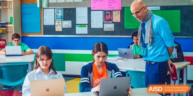A female student from Changchun American International School (CAIS) working on a laptop in a classroom with educational posters.
