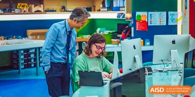 A teacher from Changchun American International School (CAIS) assisting a student working on a tablet in a technology-integrated class.