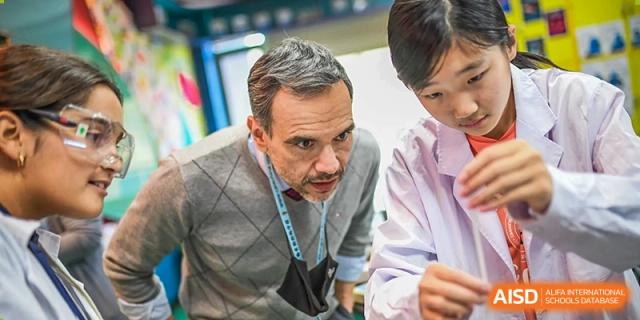 A male teacher from Changchun American International School (CAIS) engaging with a group of male students in a classroom.