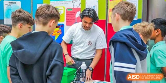 A teacher or mentor from Changchun American International School (CAIS) assisting students with a science or technology project, possibly involving robotics.