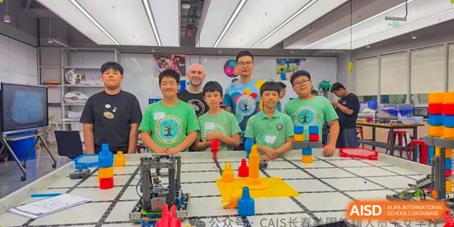 A group of students and teachers from Changchun American International School (CAIS) posing behind a small robot set up for a competition or challenge.