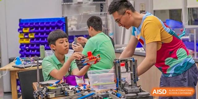 A teacher from Changchun American International School (CAIS) closely guiding a male student who is working on a construction or robotics task.