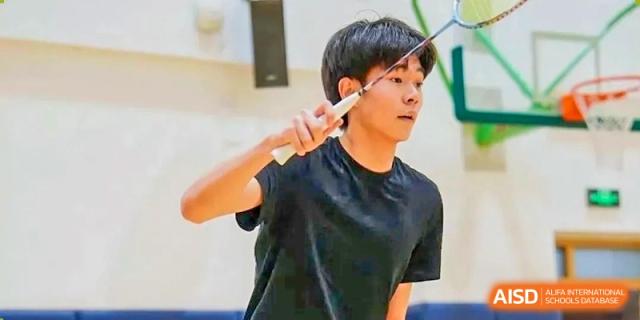 Close-up of a male student from Changchun American International School (CAIS) preparing to hit a shuttlecock during a badminton game.