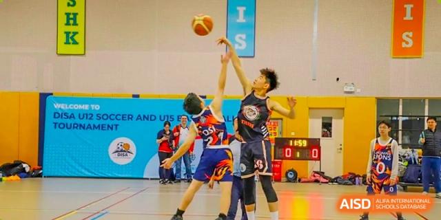 Two students intensely competing for the ball during a basketball game on an indoor court at Changchun American International School (CAIS).
