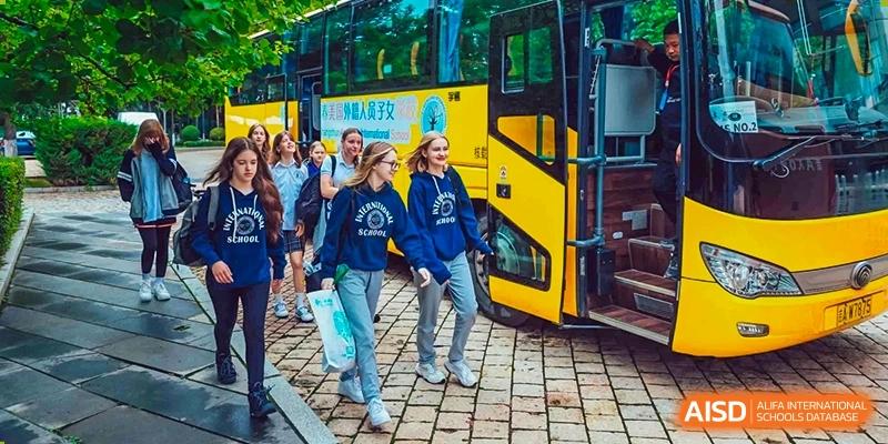 A group of students from Changchun American International School (CAIS) walking in front of a large yellow school bus, ready for a trip.