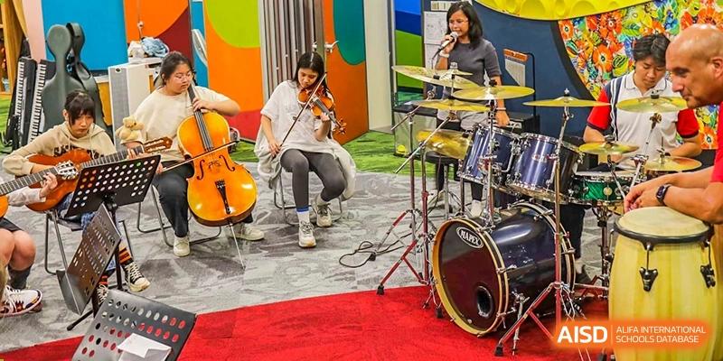 A student from Changchun American International School (CAIS) playing the cello and drums in a modern performance space.