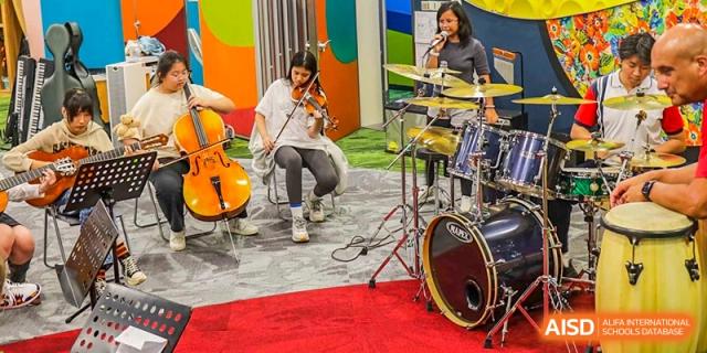 A student from Changchun American International School (CAIS) playing the cello and drums in a modern performance space.