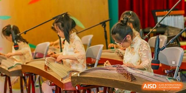 A female student from Changchun American International School (CAIS) playing a Guzheng (Chinese zither) during a cultural performance.