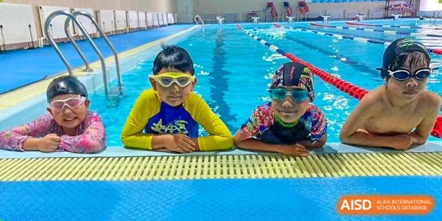Two young students from Changchun American International School (CAIS) wearing goggles and resting at the edge of the swimming pool.