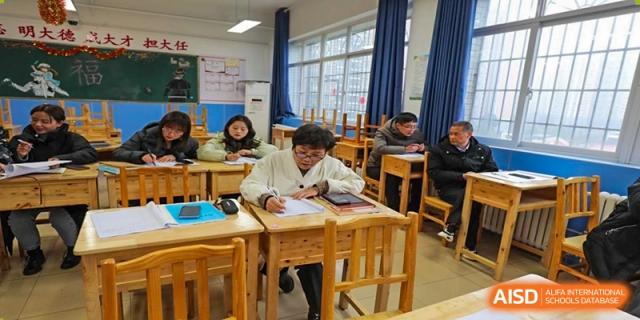 Students are seated at wooden desks in a bright classroom, working on tablets and paper assignments under natural light from large windows at Guiyang New World School.