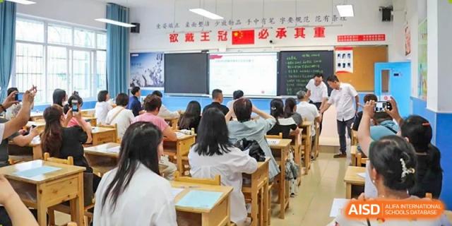 Students sit attentively in rows, facing the front of the classroom where a digital board is displaying information and text at Guiyang New World School.