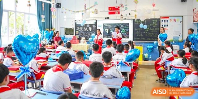 Students are watching a presentation or performance at the front of a colorful, decorated classroom, with a group of people standing up front at Guiyang New World School.