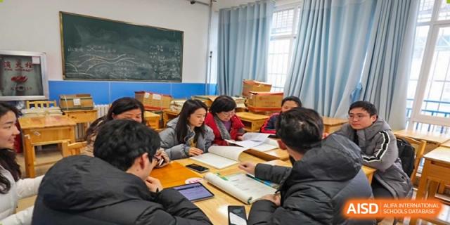 A small group of students is gathered around a table in a classroom, intensely focusing on books and tablets for their studies at Guiyang New World School.
