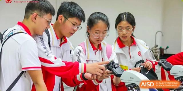 A close-up of three students in uniform huddled together, looking intently at a small electronic device or a microscope at Guiyang New World School.