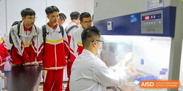 Students in uniform are watching a technician who is working with lab equipment in a modern science laboratory at Guiyang New World School.