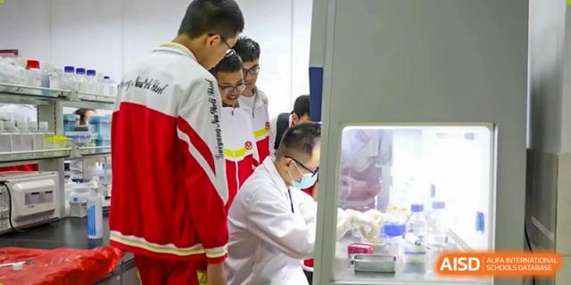 Students in red and white uniforms are observing a laboratory technician working on equipment in a clean, brightly lit lab setting at Guiyang New World School.