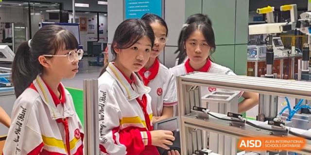 A group of female students in red and white uniforms are concentrated on an activity or looking at something on a desk or screen at Guiyang New World School.