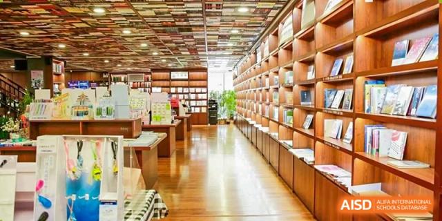 A long, well-lit aisle in a modern library or bookstore with wooden shelves filled with books on the right and a table on the left Guiyang New World School