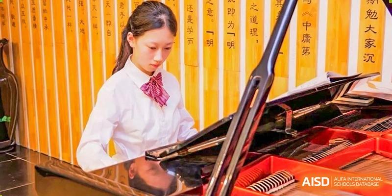A young female student focuses intently while playing the piano, demonstrating artistic development and musical talent at Guiyang New World School.