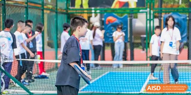 A male student concentrates while playing on the tennis court, holding his racket in preparation for a shot during a physical education class at Guiyang New World School.