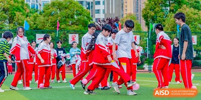 Students in red and white athletic wear navigate a team-building exercise on the green turf, focusing on coordination and cooperation at Guiyang New World School.