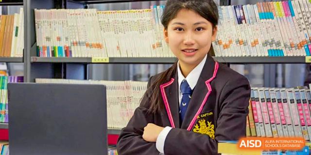 A female student in school uniform smiling confidently with her arms crossed in a library setting at Haileybury Schools, Tianjin.