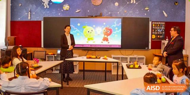 A teacher presenting a lesson with animated characters on a large screen in a bright classroom at Haileybury Schools, Tianjin.