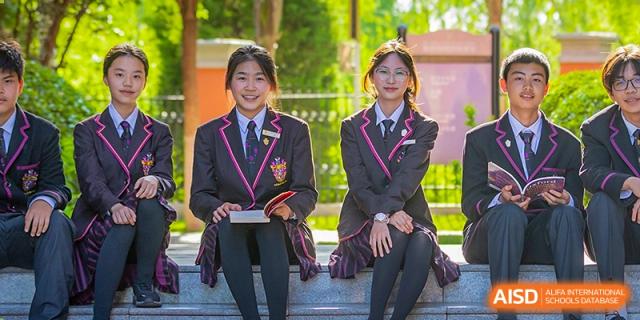 Two female students in uniform seated and smiling outdoors on the school grounds at Haileybury Schools, Tianjin.