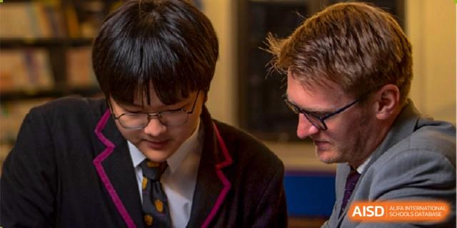 A male student wearing glasses looking down while working with a teacher or another student at Haileybury Schools, Tianjin.