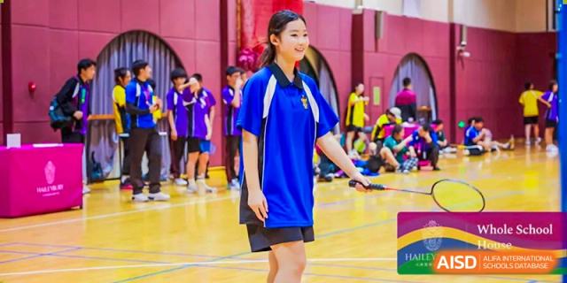 A female student in a blue sports shirt preparing to hit a shuttlecock during a badminton game at Haileybury Schools, Tianjin.