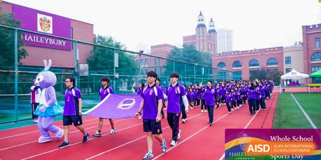 Students in purple running or marching with a purple school banner on the paved grounds at Haileybury Schools, Tianjin.