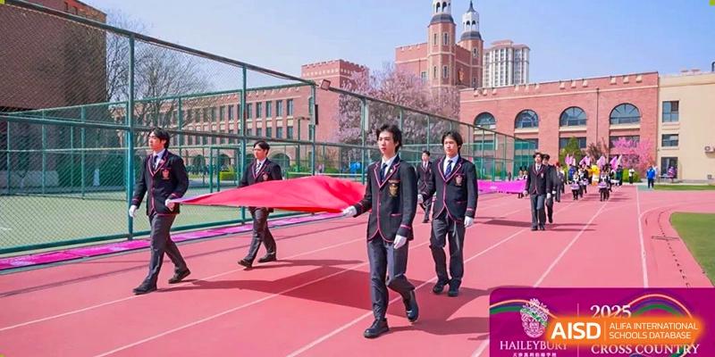 Teachers or staff in dark suits carrying a large red banner across the sports field at Haileybury Schools, Tianjin.