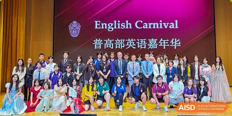 A large group photo of students and teachers posing under a sign for the "English Carnival" at Haileybury Schools, Tianjin.
