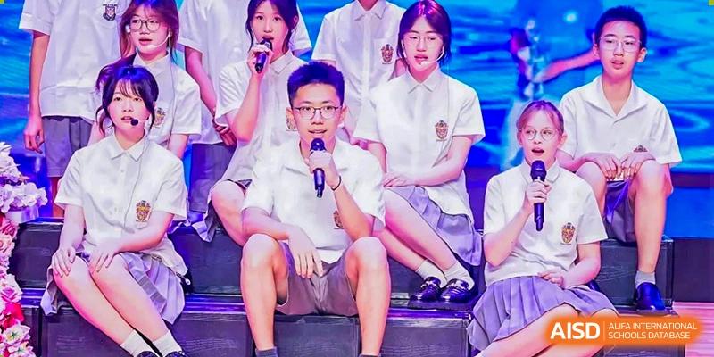 A student wearing glasses sitting and looking at the camera with other students in uniform on a stage at Haileybury Schools, Tianjin.