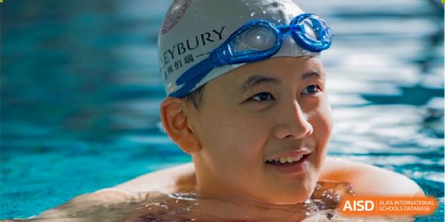 A close-up of a smiling male student wearing a swimming cap and goggles in the school pool at Haileybury Schools, Tianjin.